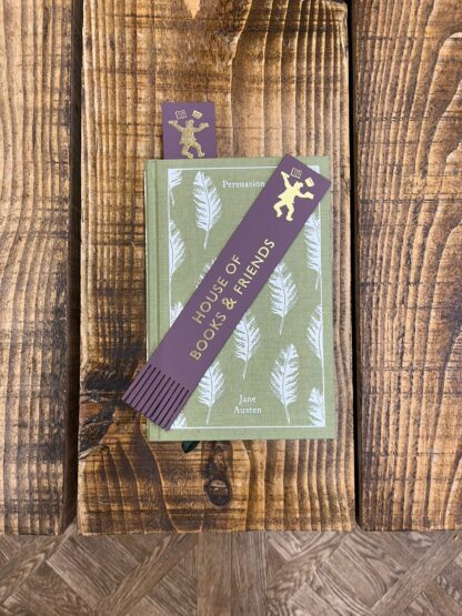 A purple book mark with the House of Books & Friends logo printed in gold foil on it. The bookmark is placed on top of a green copy of Persuasion by Jane Austen.